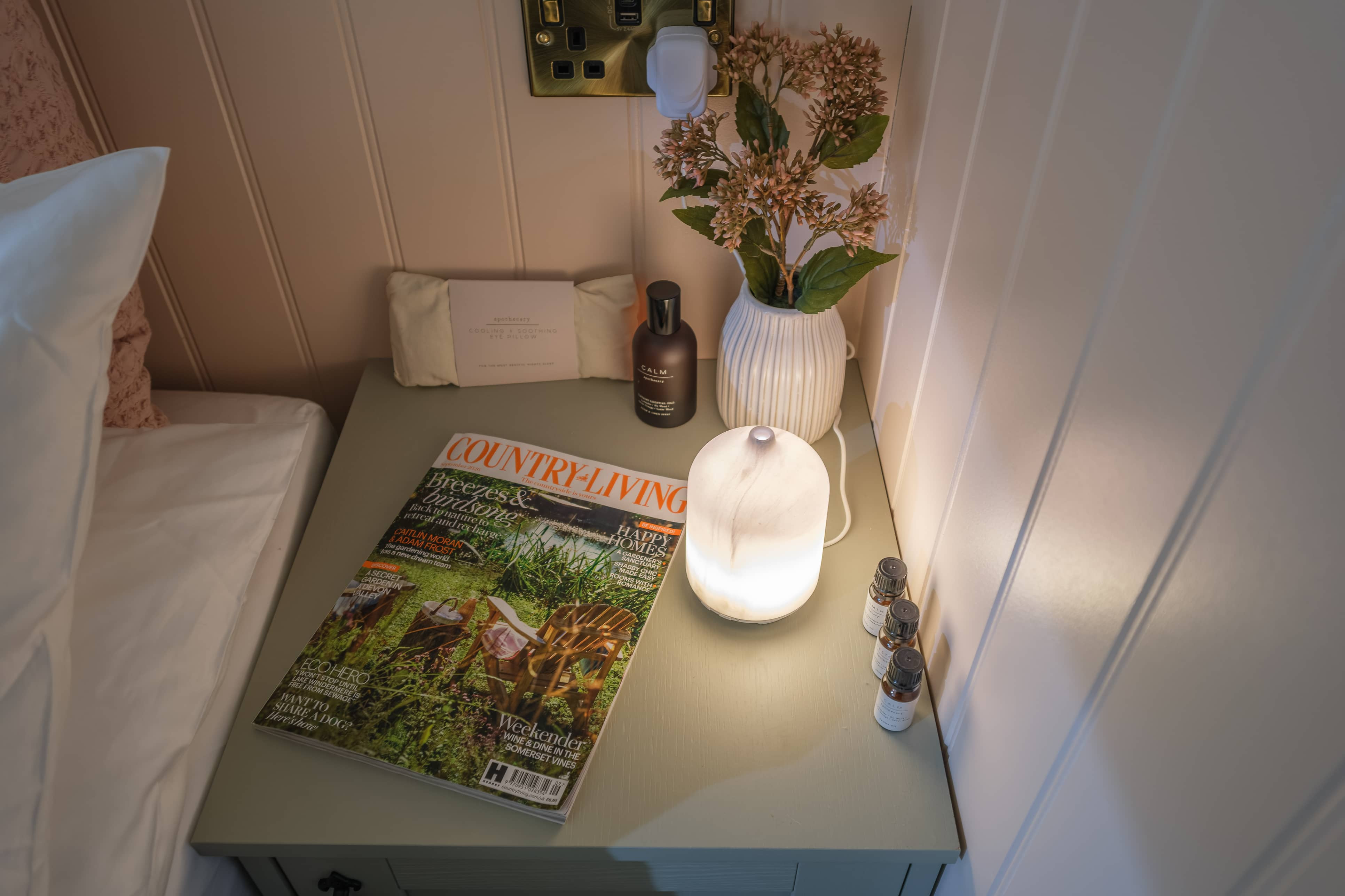 Bedside table showing Country Living magazine and an oil diffuser